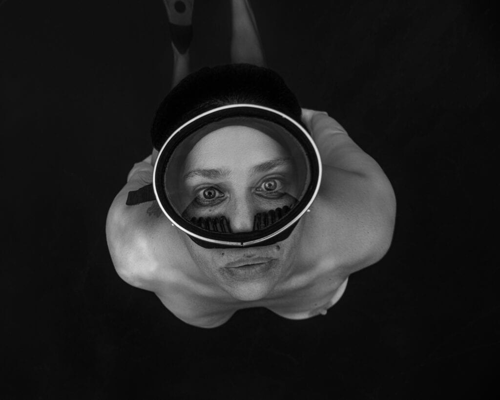 Portrait underwater noir et blanc. portrait photographié par une femme. Femme qui remonte à la surface. Gros plan sur son visage et ses yeux au travers d'un masque vintage. On voit très peu son sein gauche, mais pas le droit car mastectomie