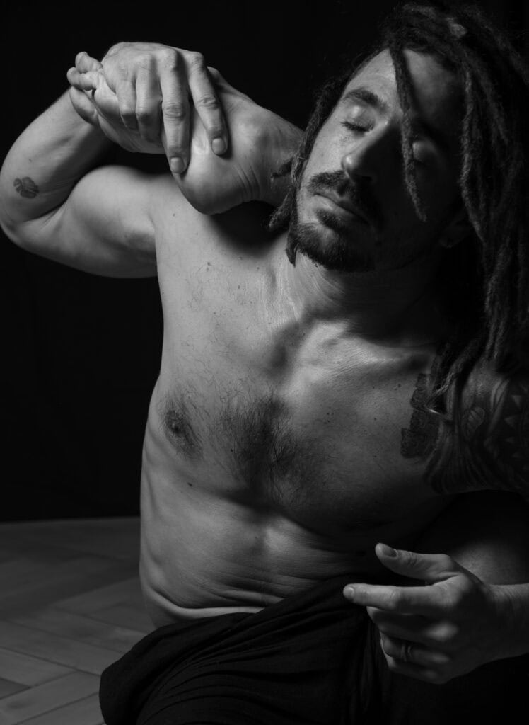 Portrait professionnel noir et blanc. Portrait photographié par une femme. pratiquant du yoga, prise de son pied droit sur son épaule droite. Il a les yeux fermés. On voit son torse. p