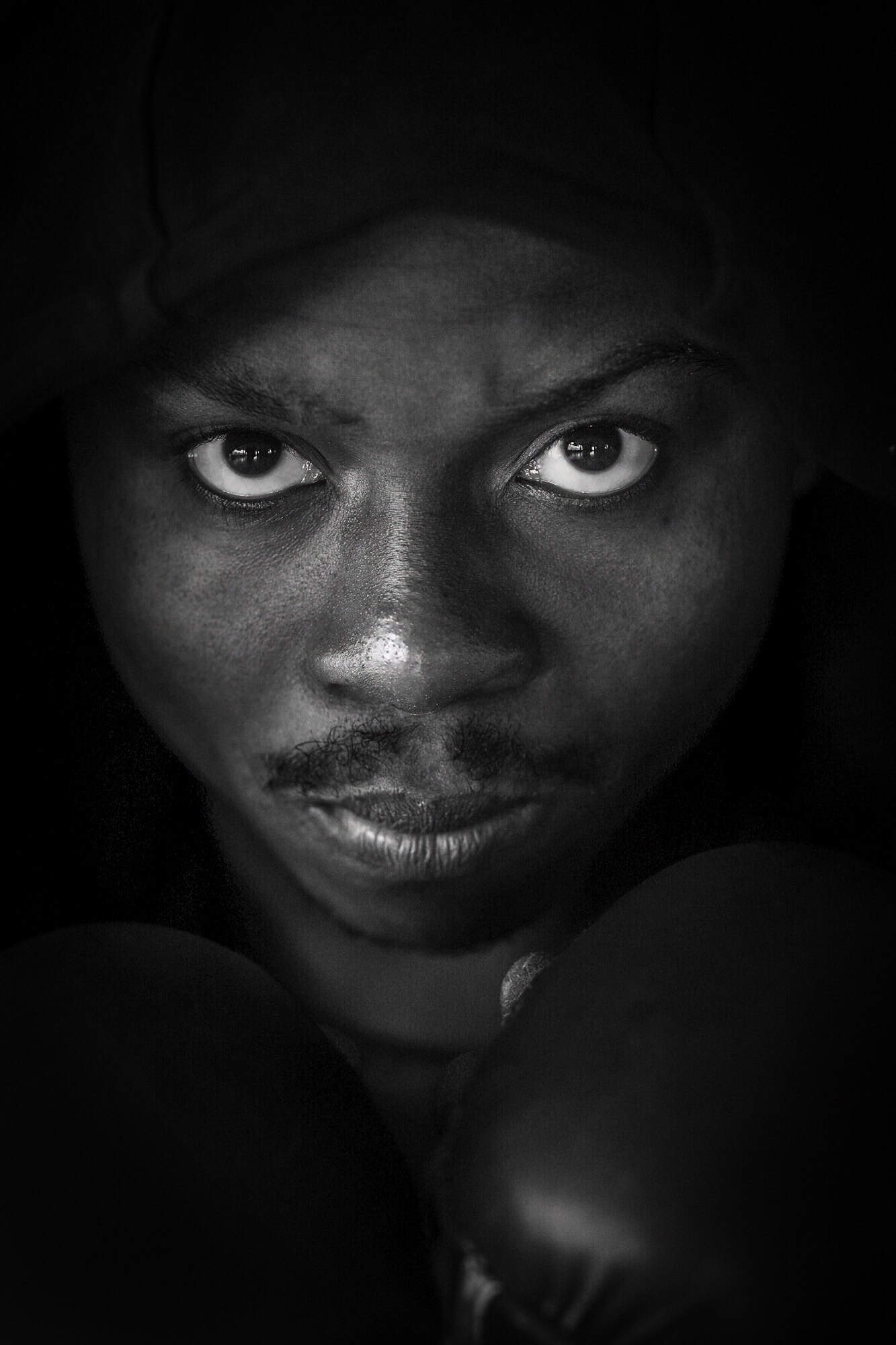 Portrait professionnel en noir et blanc. Portrait photographié par une femme. Il s'agit d'un gros plan d'un boxeur. C'est une personne de couleur de peau noire. Son regard est très très intense.