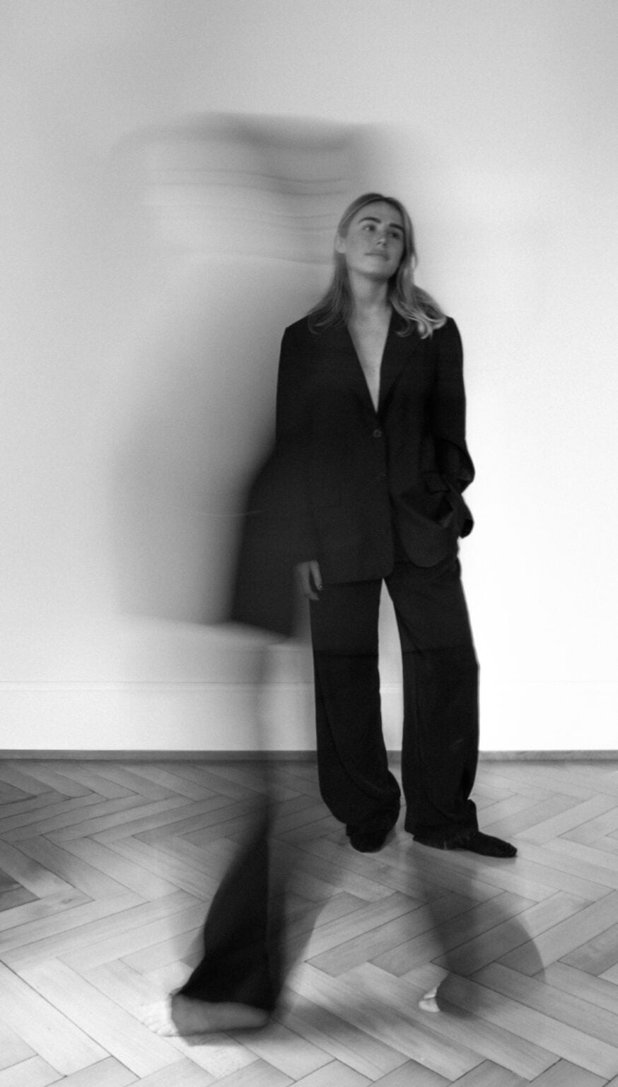 Portrait artistique créatif en noir et blanc, photographié par une femme. Jeune femme debout face à objectif. Autre femme passe devant et est floue. Photographie avec du grain