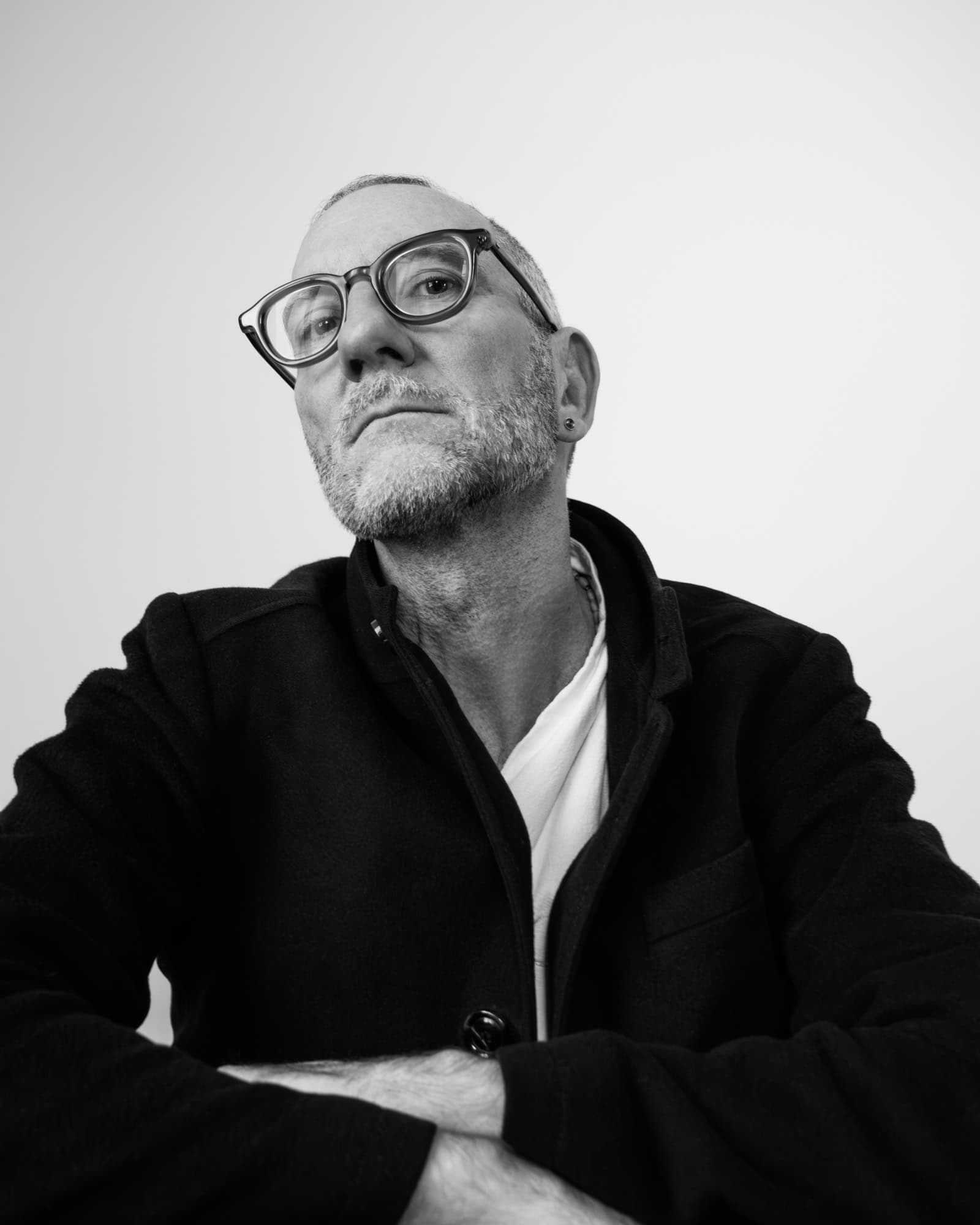 Portrait professionnel en noir et blanc. LA photo est prise en contre-plongé. Homme porte un tshirt blanc avec une veste noire. Il porte également des lunettes.