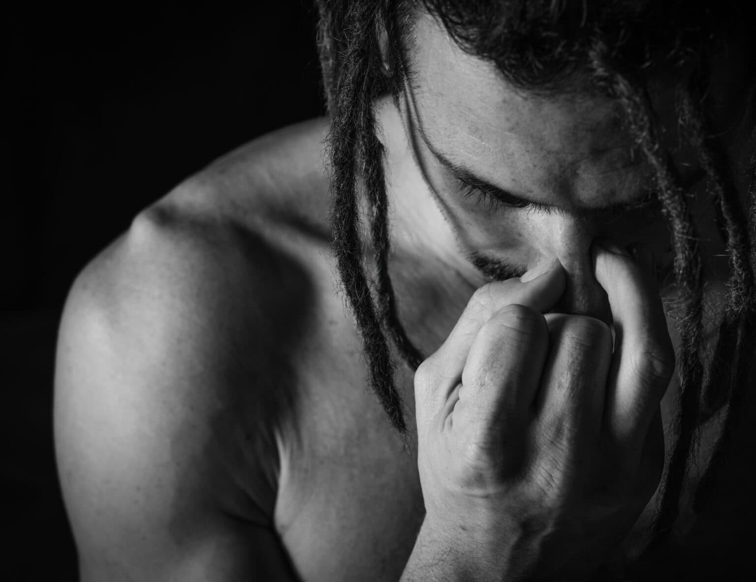 Portrait professionnel en noir et blanc. portrait photographié par une femme. GRos plan sur le visage et main droit. Homme pratiquant la méditation, la respiration en fermant ses narines avec sa main droite. Il a le torse nu.