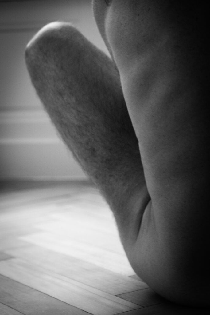 nu artistique masculin en noir et blanc, portrait intimiste photographié par une femme. Homme vu de dos , seul son côté gauche se voit, ainsi que sa cuisse face antérieure.