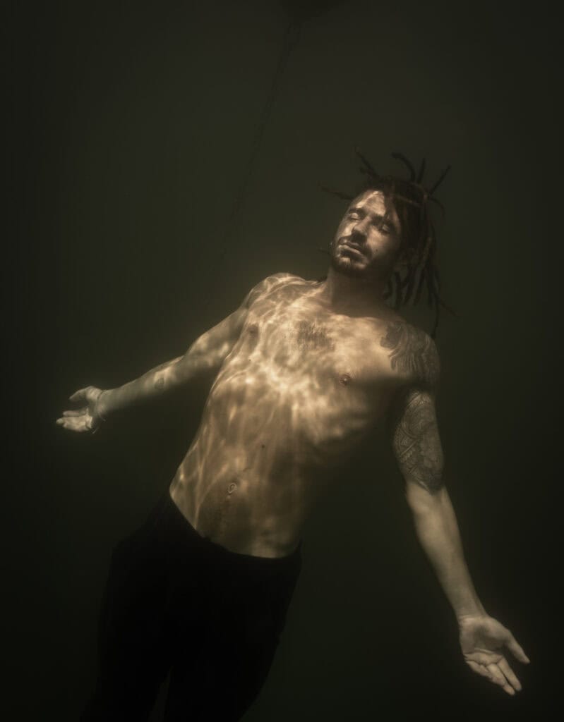Portrait underwater en couleur. portrait photographié par une femme. Il s'agit d'un homme avec les yeux fermés tourné vers la surface. Il a les bras ouverts et le torse tourné vers la lumière.